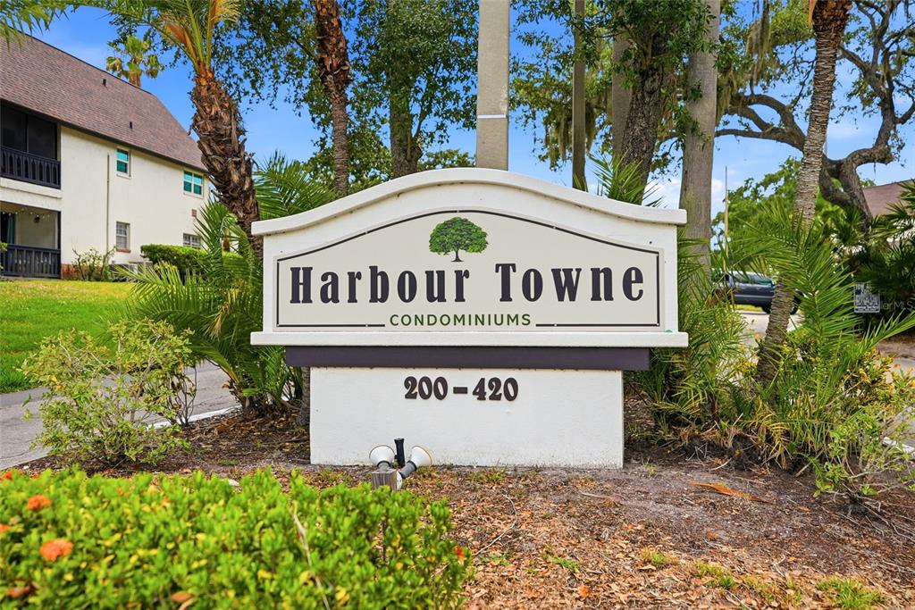 A sign for Harbour Towne Condominiums stands outdoors surrounded by palm trees and landscaping — 316 N BAYSHORE BOULEVARD UNIT 208, CLEARWATER, FL