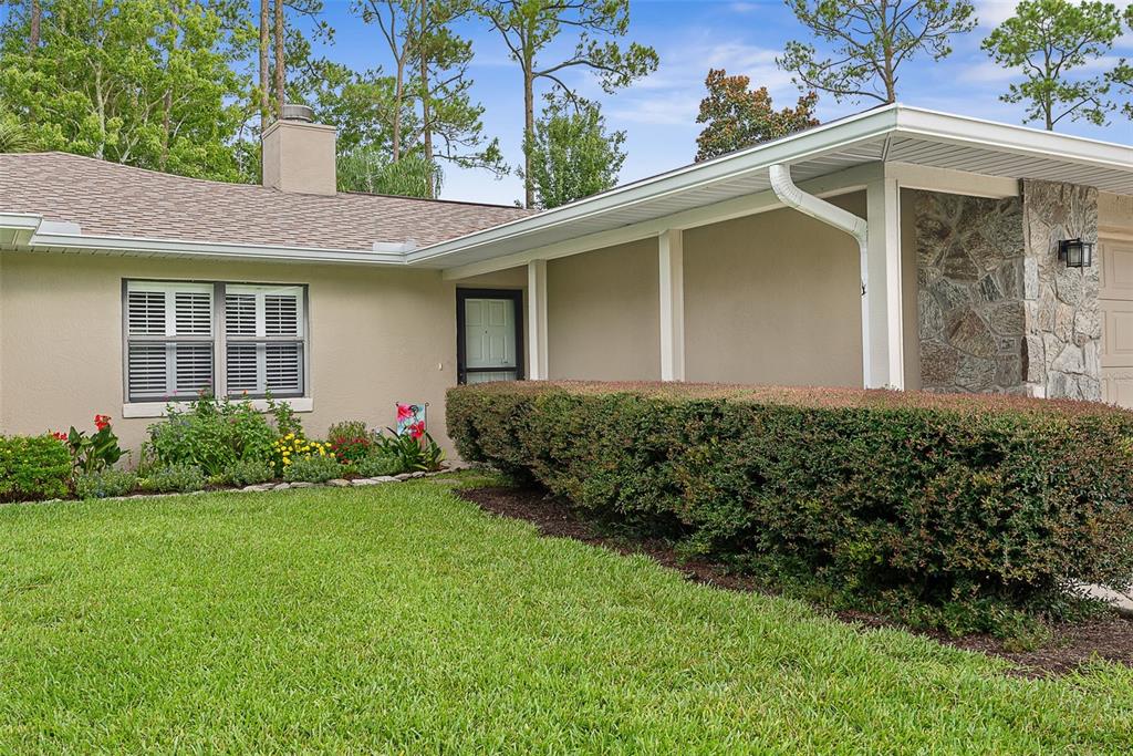 A single-story house exterior features a stone facade, a covered porch, and a manicured hedge — 49 BANNERWOOD LANE, PALM COAST, FL