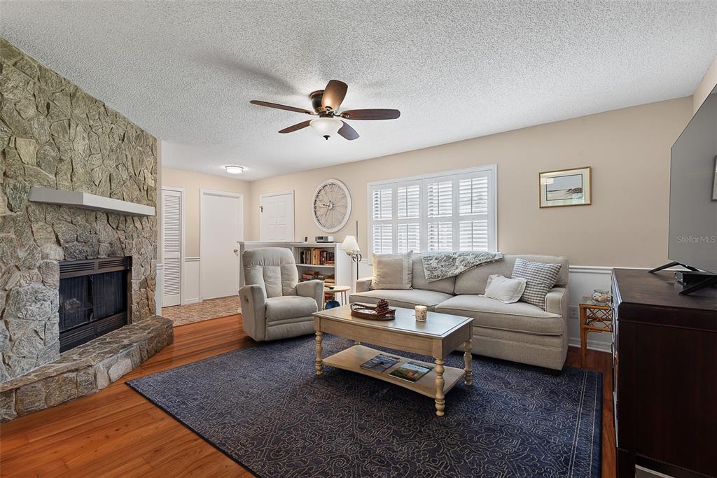A living room features a stone fireplace, hardwood floors, a ceiling fan, and neutral furniture — 49 BANNERWOOD LANE, PALM COAST, FL