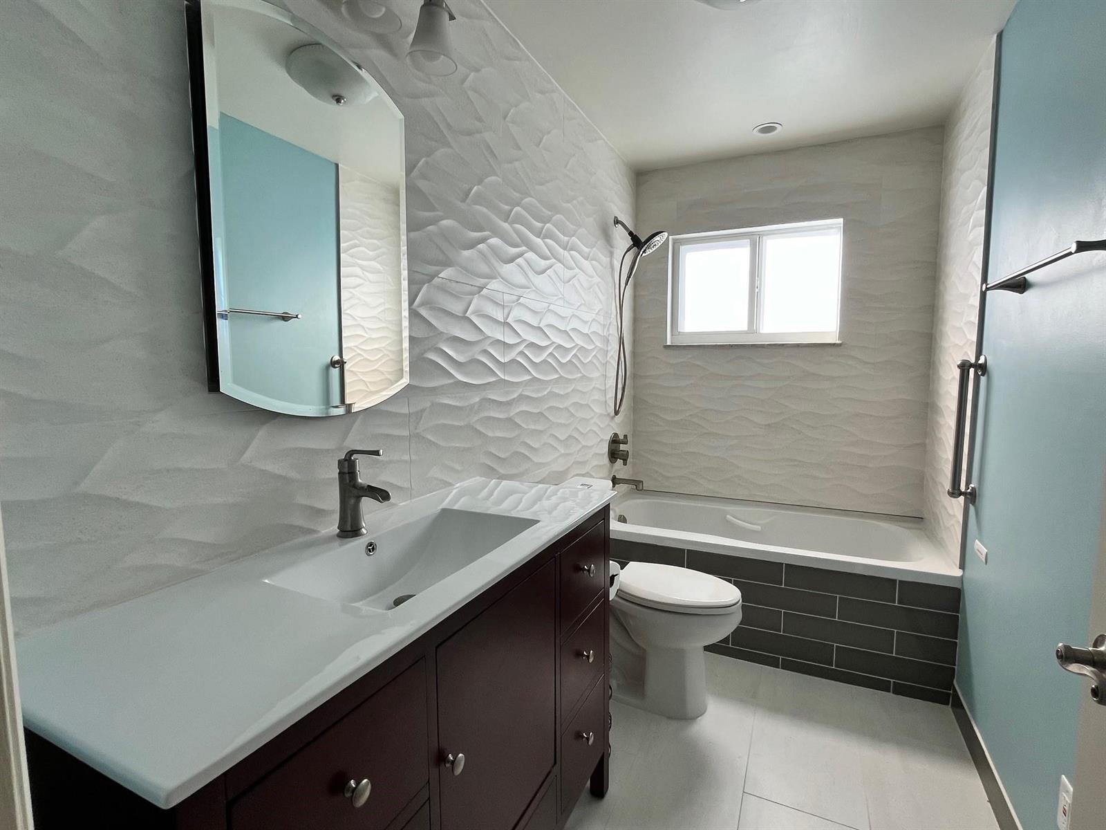 A bathroom features a dark wood vanity, a textured white wall, and a bathtub surround — 3040 NW 1st Avenue, Pompano Beach FL 33064, POMPANO BEACH, FL