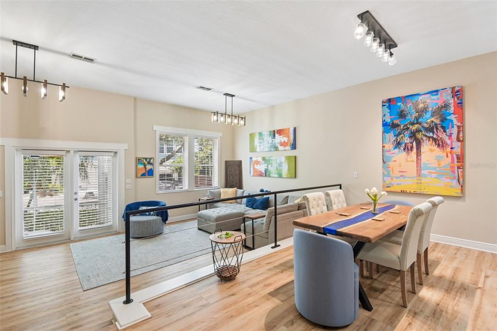 An open-concept living and dining area features light wood flooring, a metal railing, and artwork — 131 ATHENIAN WAY, TARPON SPRINGS, FL