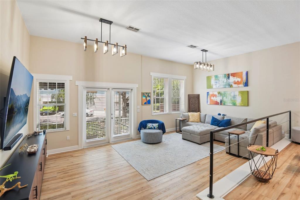 A living room features light wood flooring, a gray sectional sofa, and two modern chandeliers — 131 ATHENIAN WAY, TARPON SPRINGS, FL