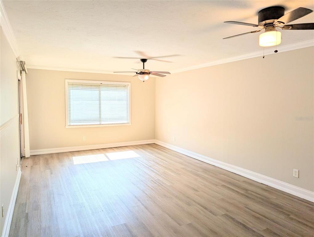 An empty room features light wood-look flooring, beige walls, and two ceiling fans — 3700 S OSPREY AVENUE UNIT 212, SARASOTA, FL