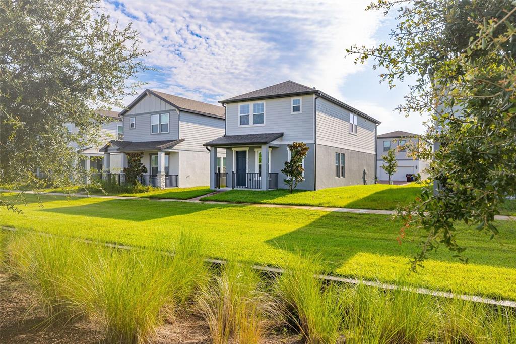 Two-story suburban houses with light gray siding and front porches sit along a grassy lawn — 4629 CROSS PRAIRIE PARKWAY, ST CLOUD, FL