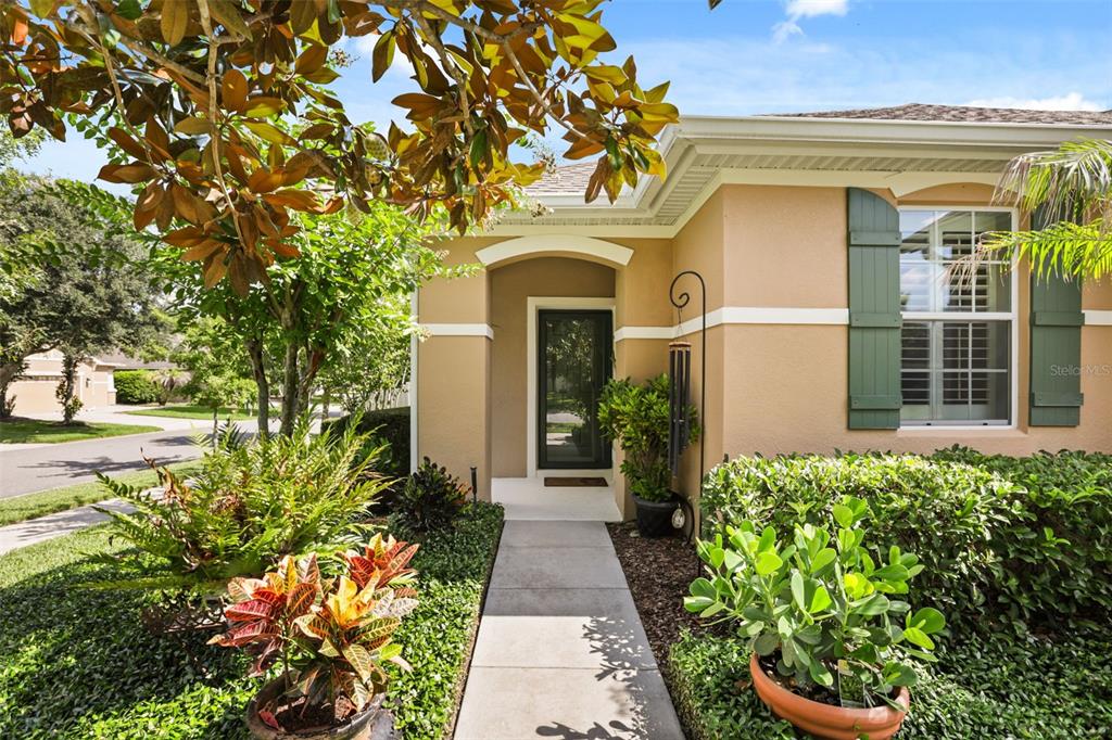 A concrete walkway leads to the front entrance of a tan house with green shutters — 30119 TOKARA TERRACE, MOUNT DORA, FL