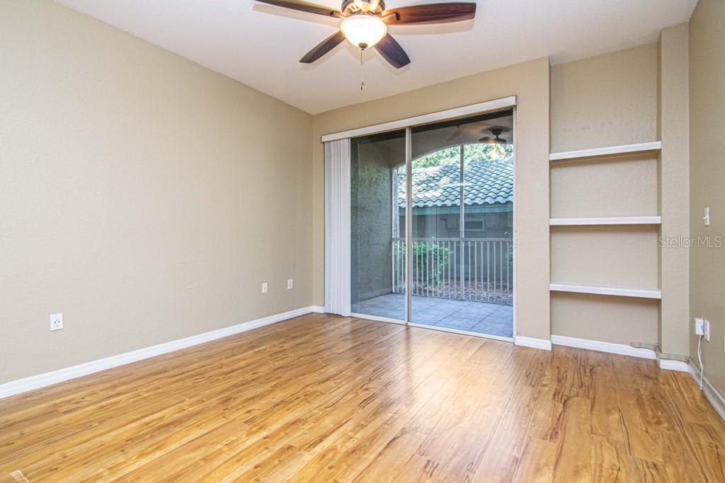 An empty room with wood-look flooring, a ceiling fan, built-in shelves, and a sliding glass door — 5713 LEGACY CRESCENT PLACE UNIT 101, RIVERVIEW, FL