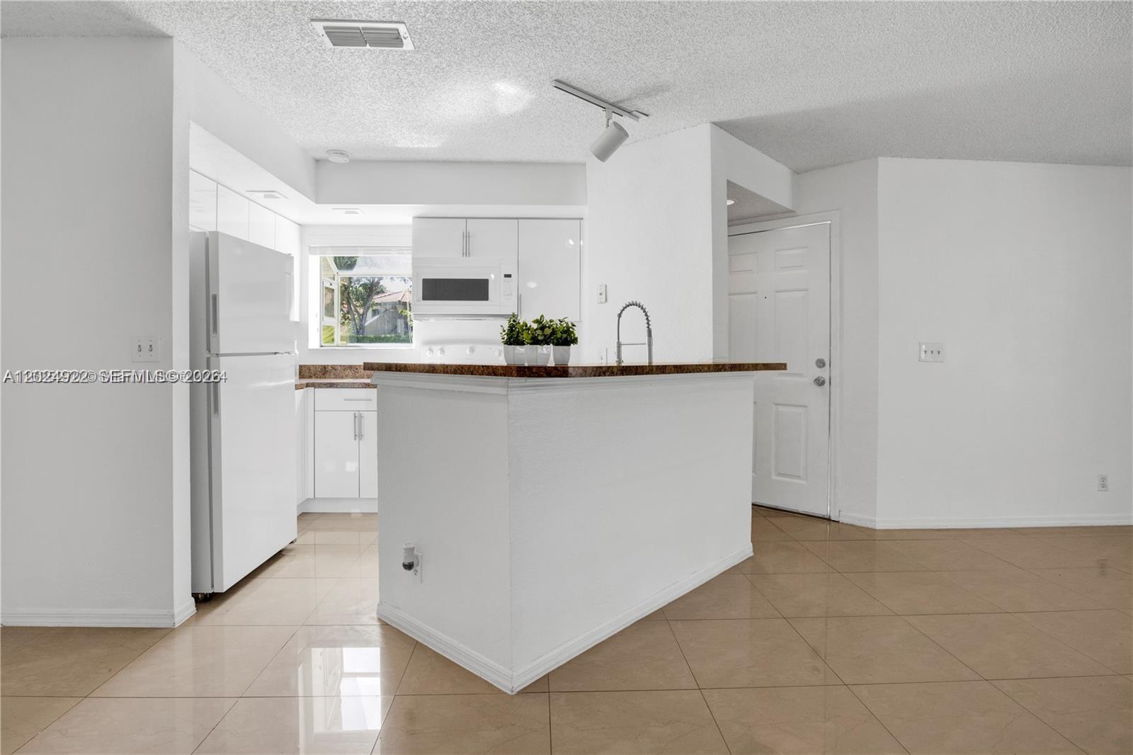A white kitchen features a granite-topped island, light tile flooring, and a white refrigerator — 3420 N Pinewalk Dr N # 717, Margate FL 33063, MARGATE, FL