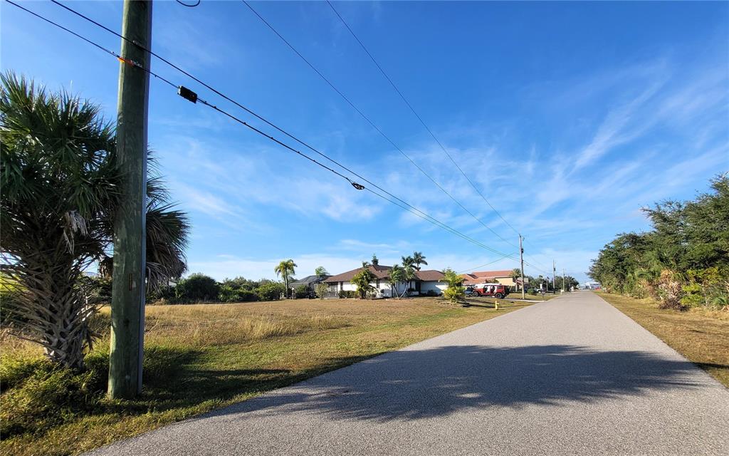 A vacant grassy lot sits beside a paved road with a house in the background — 9620 PRESIDENT CIRCLE, PORT CHARLOTTE, FL