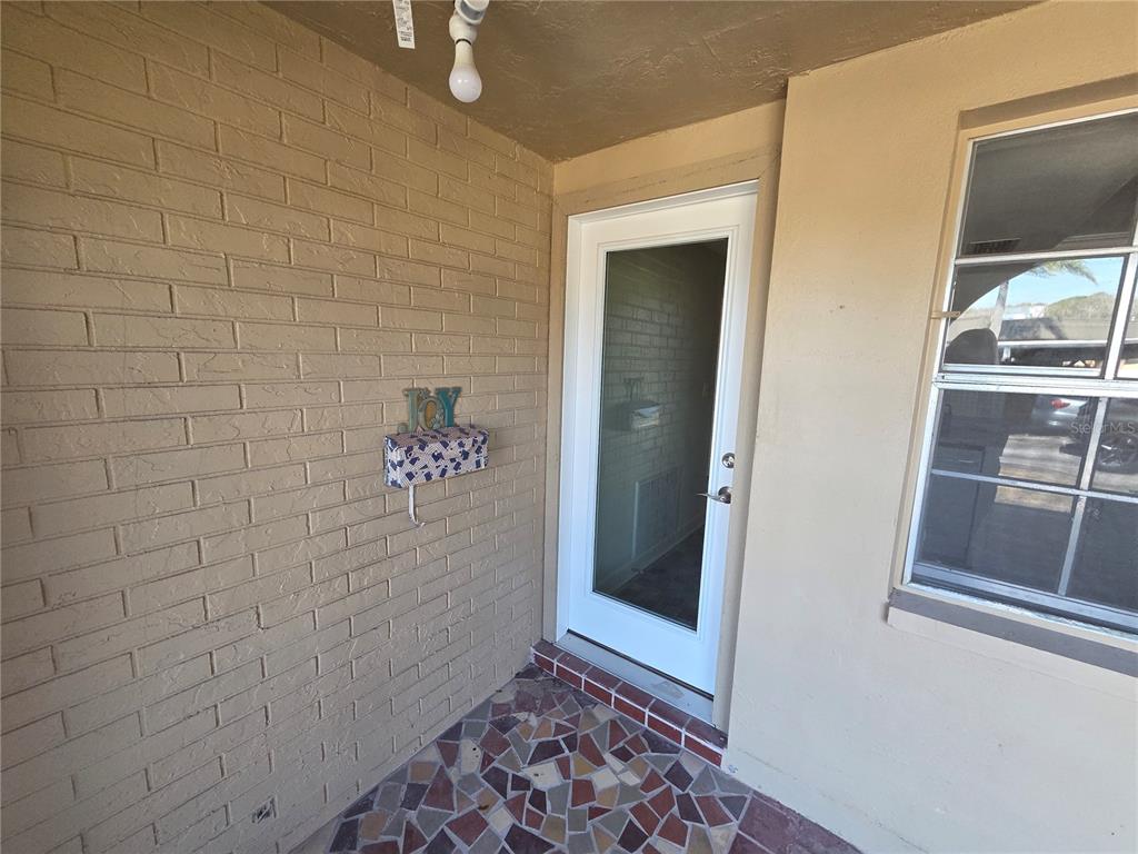 A covered entryway features a brick wall, a glass-paneled door, and a mosaic tile floor — 4120 STRATFORD DRIVE, NEW PORT RICHEY, FL