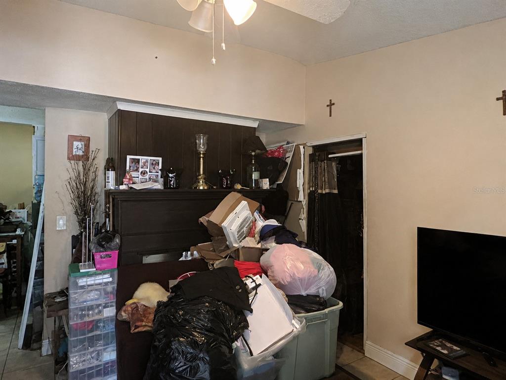 A cluttered living room features a dark wood fireplace mantel, tile flooring, and a ceiling fan — 4710 ROBBINS AVENUE, ORLANDO, FL