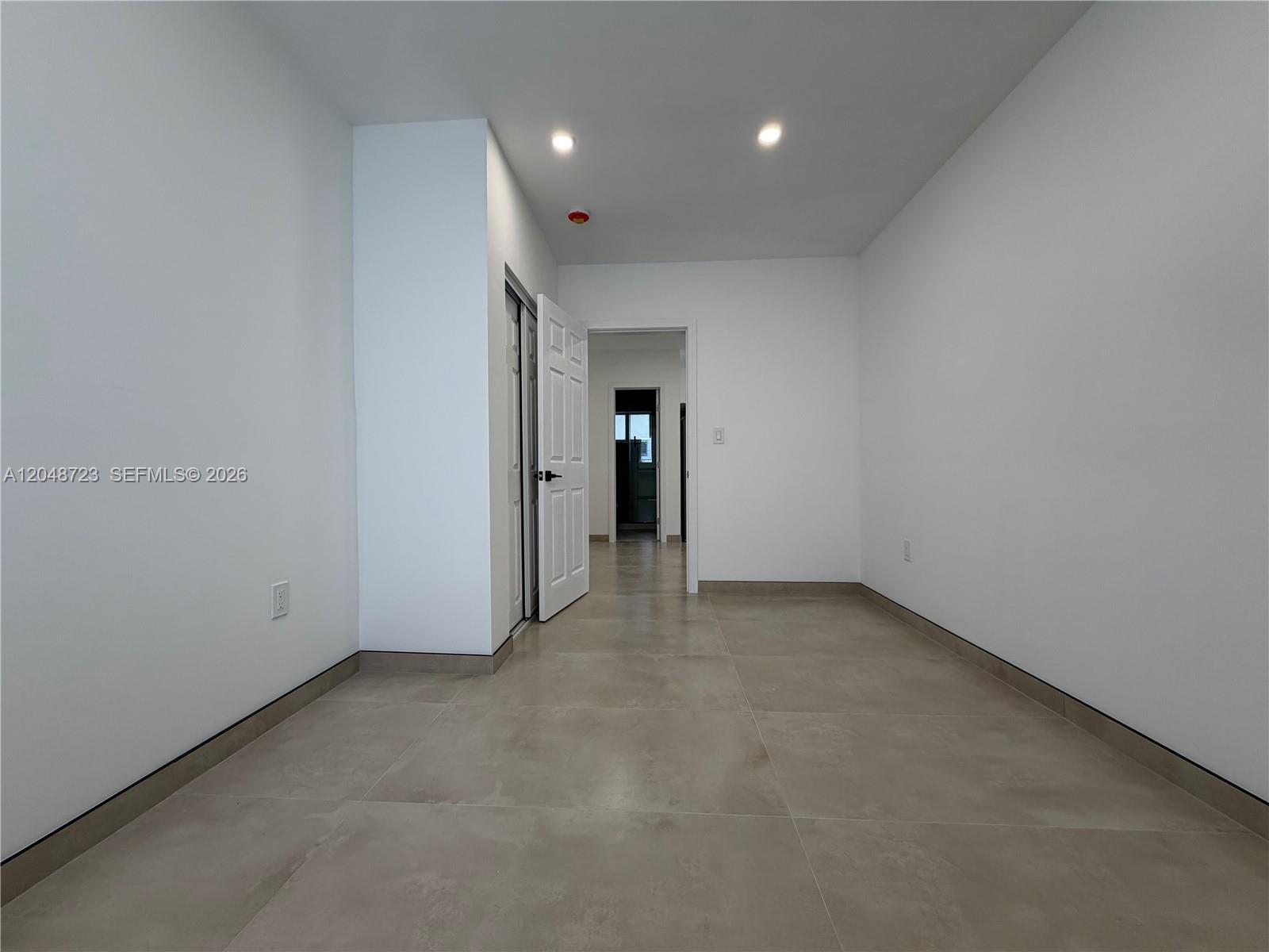 An empty room with white walls, large beige floor tiles, and an open doorway — 1235 Normandy Dr # 7, Miami Beach FL 33141, MIAMI BEACH, FL
