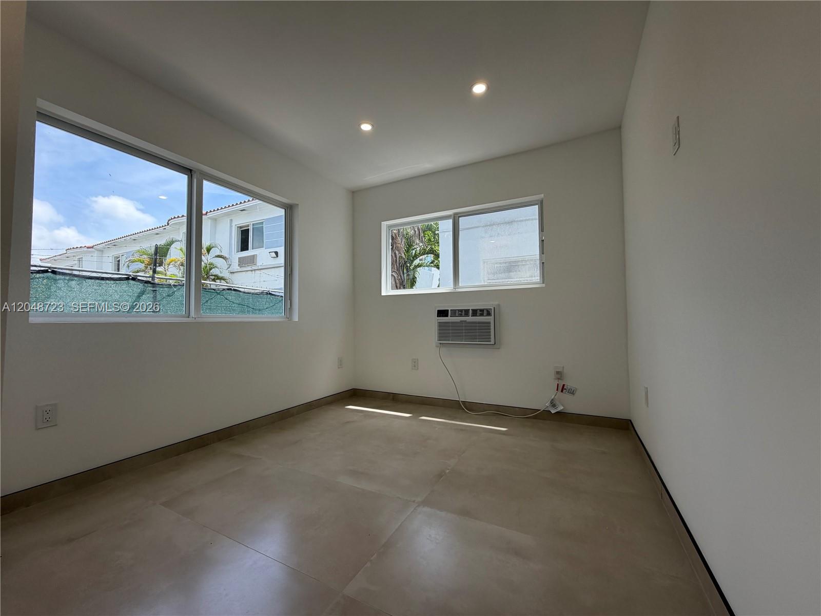 An empty room features white walls, large windows, tile flooring, and a wall-mounted air conditioner — 1235 Normandy Dr # 7, Miami Beach FL 33141, MIAMI BEACH, FL