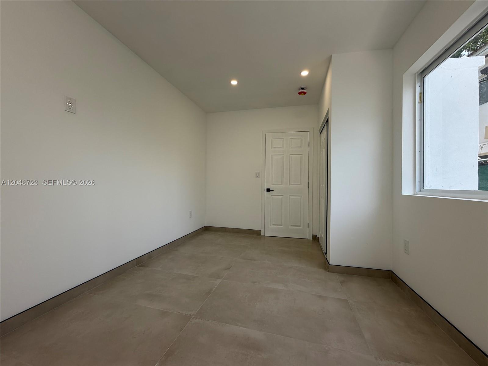 An empty room with white walls, tile flooring, a single door, and a window — 1235 Normandy Dr # 7, Miami Beach FL 33141, MIAMI BEACH, FL