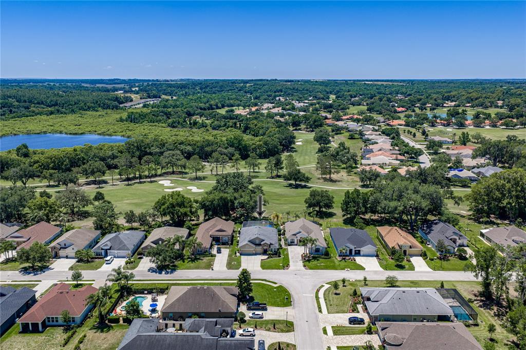 An aerial view shows a residential neighborhood with houses bordering a golf course and lake — 34530 HEAVENLY LANE, DADE CITY, FL