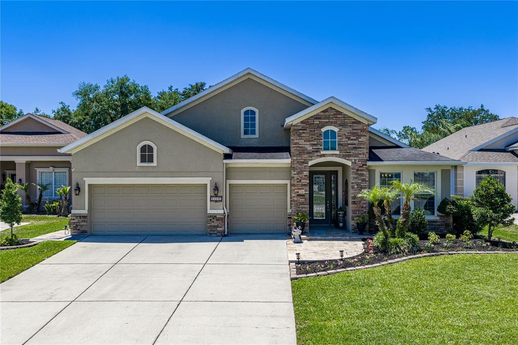 A single-story suburban house with a stone-accented entryway, two-car garage, and a concrete driveway — 34530 HEAVENLY LANE, DADE CITY, FL