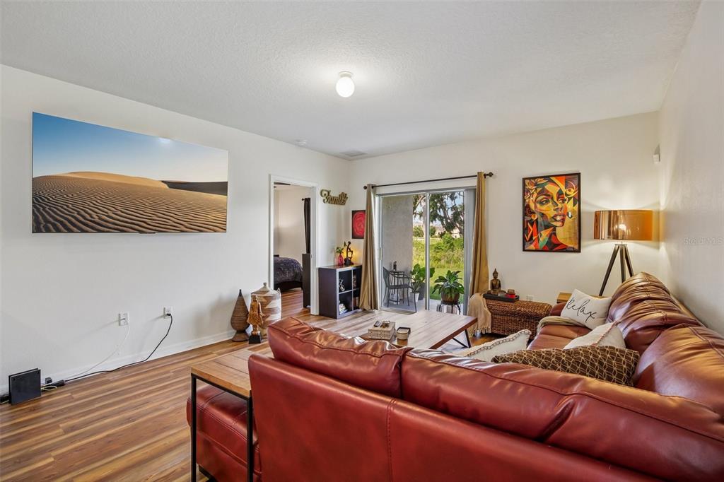 A living room features a red leather sectional, wood-look flooring, and a wall-mounted television — 11008 LELAND GROVES DRIVE, RIVERVIEW, FL
