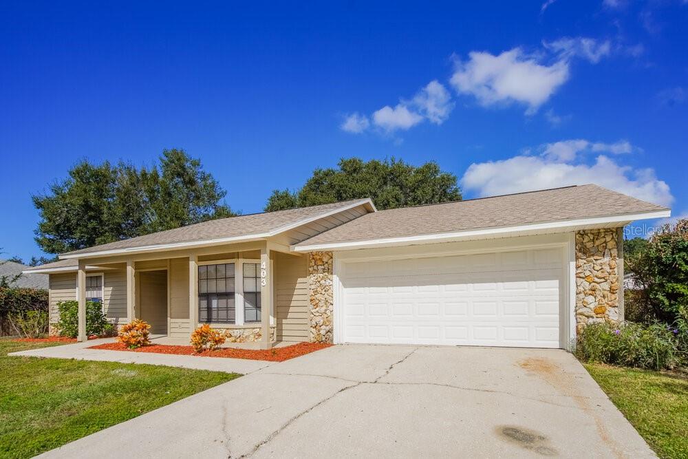 A single-story house with tan siding, a stone facade, and a two-car garage — 403 BLUEBERRY DRIVE, EUSTIS, FL