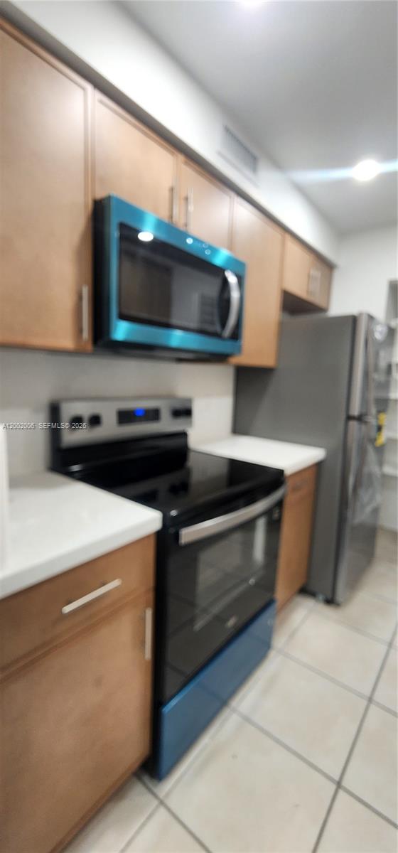 A kitchen features wooden cabinets, a black stove, a microwave, and a stainless steel refrigerator — 500 NE 2nd St # 213, Dania Beach FL 33004, DANIA BEACH, FL