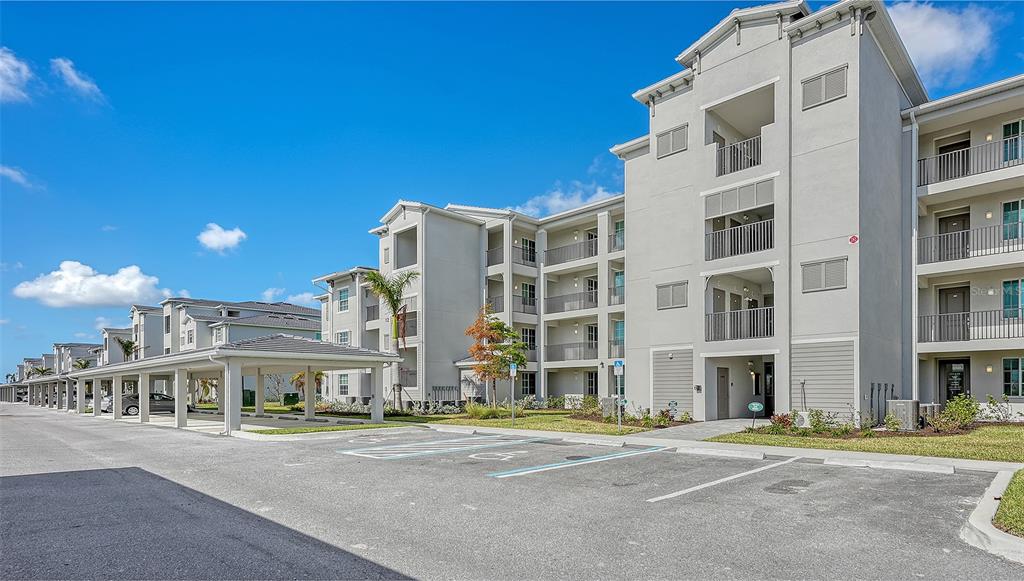 A multi-story apartment building with covered parking spaces and a paved parking lot in front — 12140 WELLEN GOLF STREET UNIT 203, VENICE, FL