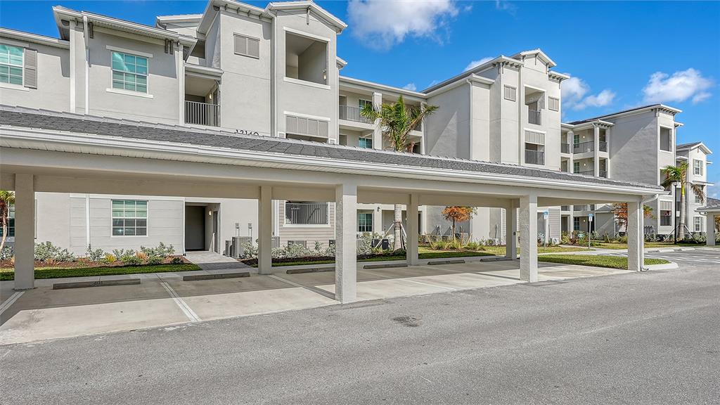 A multi-story apartment building features a covered parking structure in the foreground — 12140 WELLEN GOLF STREET UNIT 203, VENICE, FL