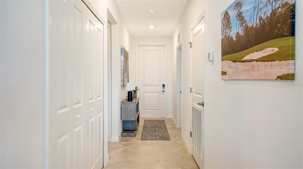 A bright hallway features tile flooring, white doors, a small console table, and wall art — 12140 WELLEN GOLF STREET UNIT 203, VENICE, FL