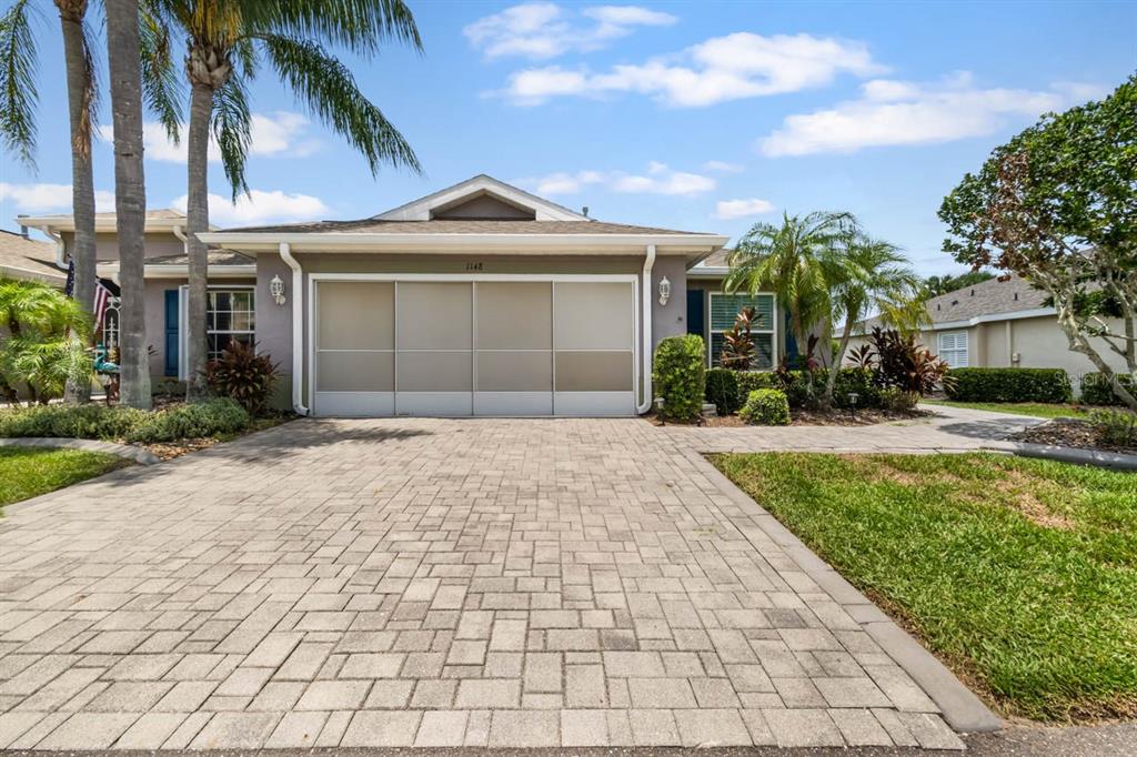 A single-story house with a paved driveway, a three-panel garage door, and palm trees — 1148 CORINTH GREENS DRIVE, SUN CITY CENTER, FL
