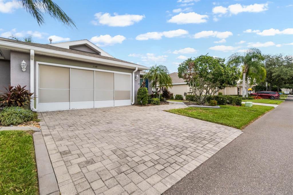 A paved driveway leads to a house with a white screen door over the garage — 1148 CORINTH GREENS DRIVE, SUN CITY CENTER, FL