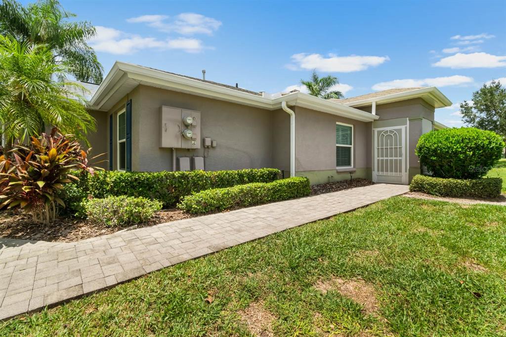 A paved walkway leads to the front entrance of a single-story house with tan stucco — 1148 CORINTH GREENS DRIVE, SUN CITY CENTER, FL