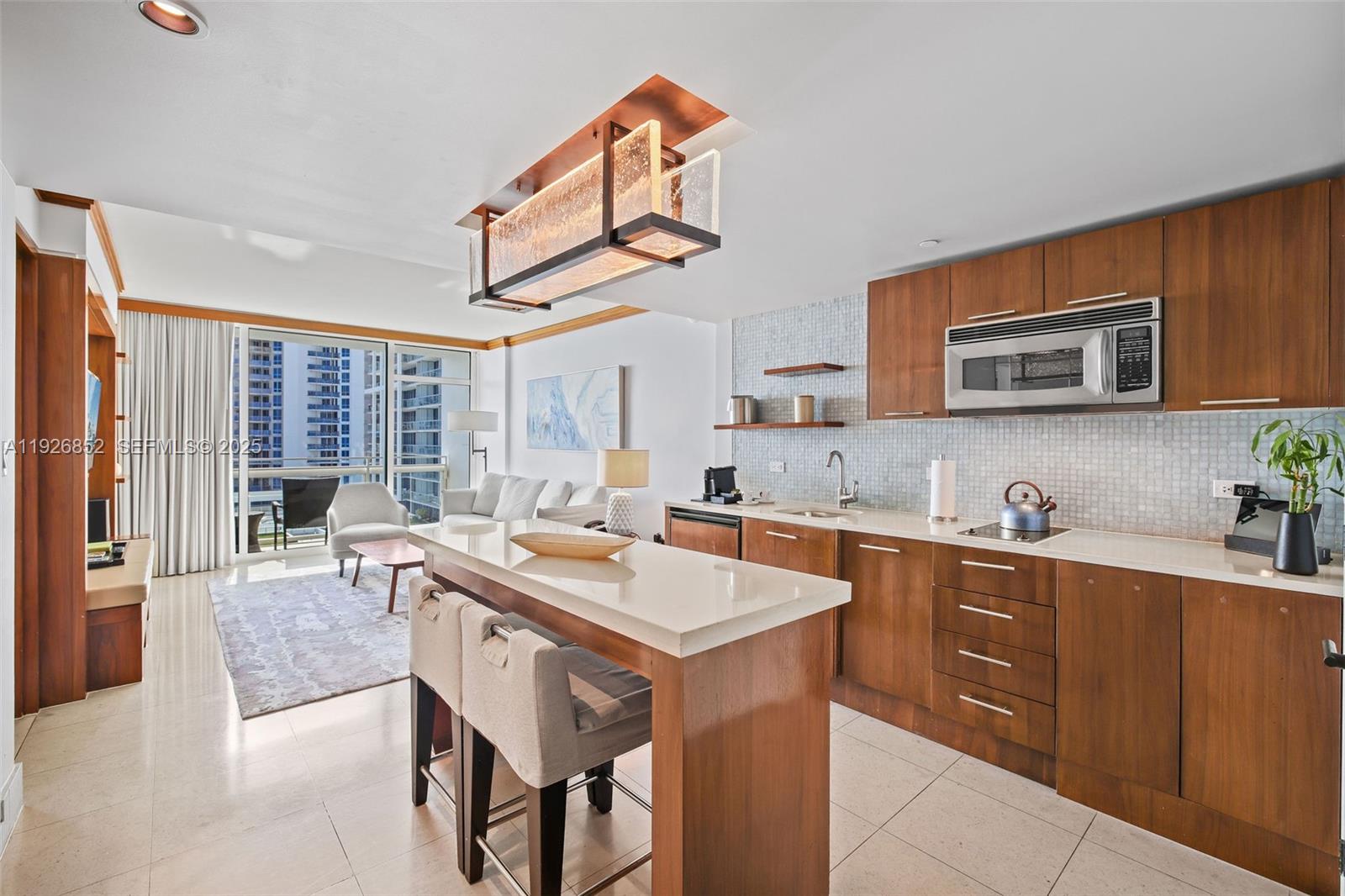 A modern kitchen with wood cabinets and a breakfast bar opens into a living area — 6801 Collins Ave, Miami Beach FL 33141, MIAMI BEACH, FL