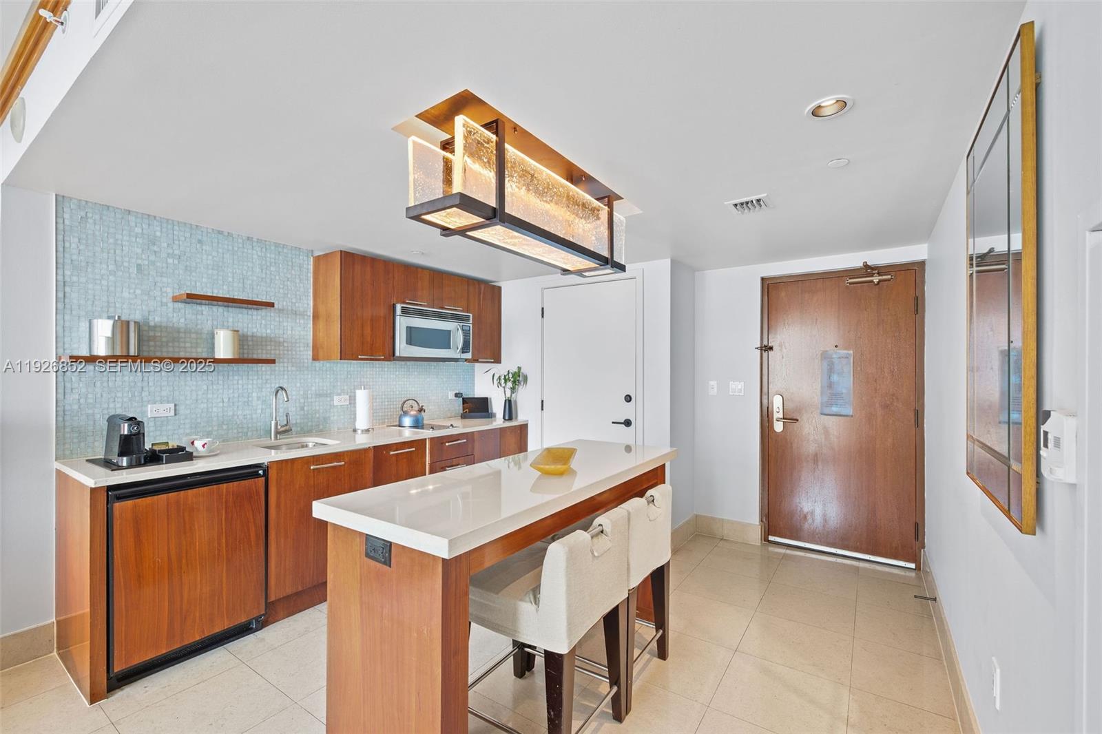 A kitchen features wood cabinetry, a white countertop island, and a light blue tiled backsplash — 6801 Collins Ave, Miami Beach FL 33141, MIAMI BEACH, FL