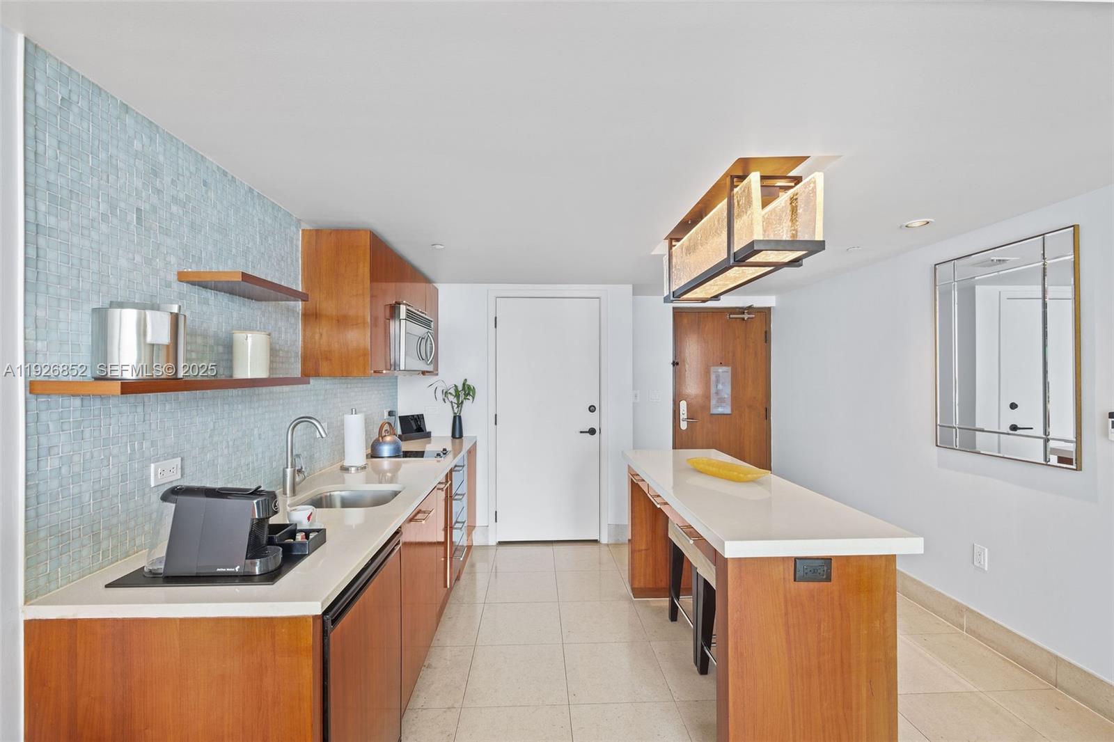 A kitchen features wood cabinetry, a light blue tiled backsplash, and a central island — 6801 Collins Ave, Miami Beach FL 33141, MIAMI BEACH, FL