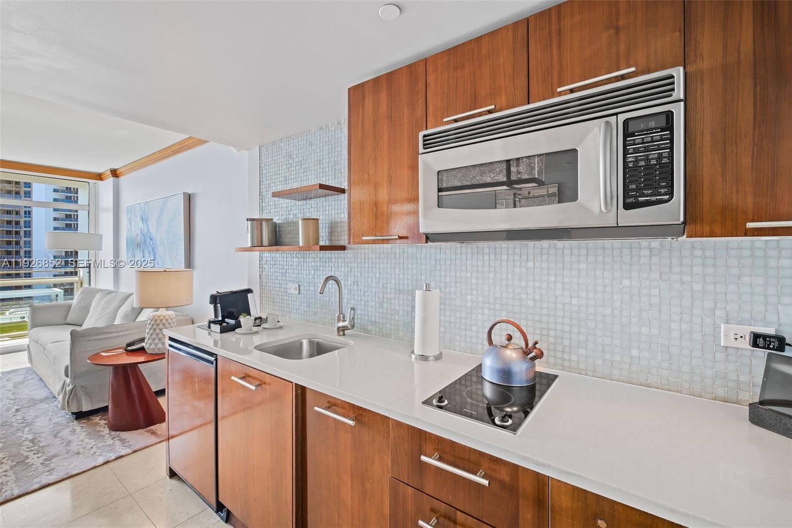 A kitchenette with wood cabinets, a microwave, a small sink, and a cooktop — 6801 Collins Ave, Miami Beach FL 33141, MIAMI BEACH, FL