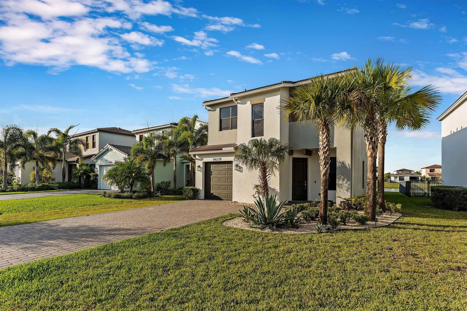 A two-story suburban house with a paved driveway, palm trees, and a small front yard — 16235 Sandy Shore Drive, Westlake FL 33470, WESTLAKE, FL