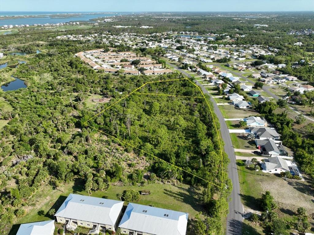 An aerial view shows a vacant, tree-covered lot outlined in yellow next to a road — 6700-6730 GASPARILLA PINES BOULEVARD, ENGLEWOOD, FL