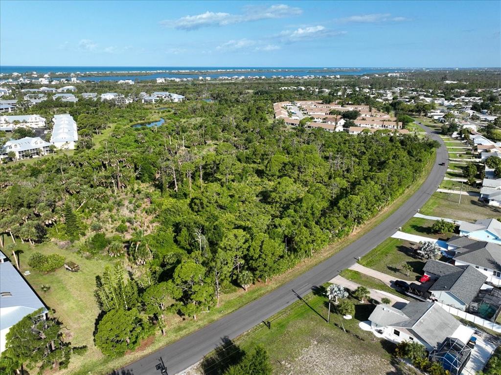 An aerial view shows a wooded vacant lot bordered by a road and residential homes — 6700-6730 GASPARILLA PINES BOULEVARD, ENGLEWOOD, FL