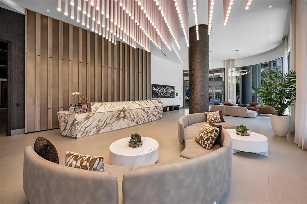 A modern lobby features a marble reception desk, curved sofas, and hanging cylindrical light fixtures — 275 1ST AVENUE S UNIT 3503, ST PETERSBURG, FL