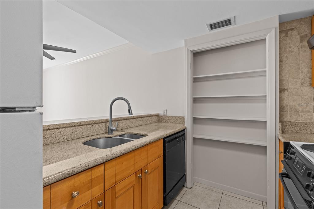 A kitchen features wood cabinets, granite countertops, a stainless steel sink, and open wall shelving — 829 1ST STREET S UNIT 3B, JACKSONVILLE BEACH, FL