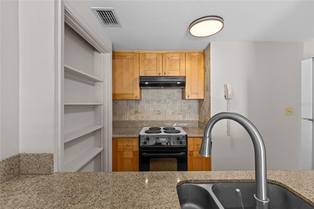 A kitchen features light wood cabinets, a tiled backsplash, a black stove, and granite countertops — 829 1ST STREET S UNIT 3B, JACKSONVILLE BEACH, FL