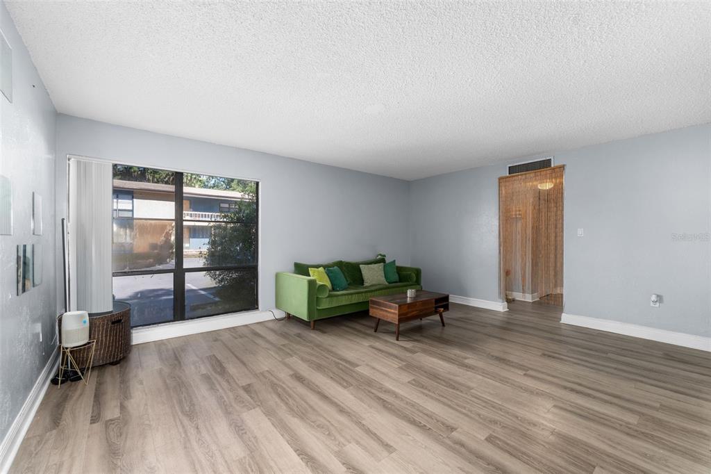 A living room with light gray walls, wood-look flooring, a green sofa, and a large window — 2811 SW ARCHER ROAD UNIT P131, GAINESVILLE, FL