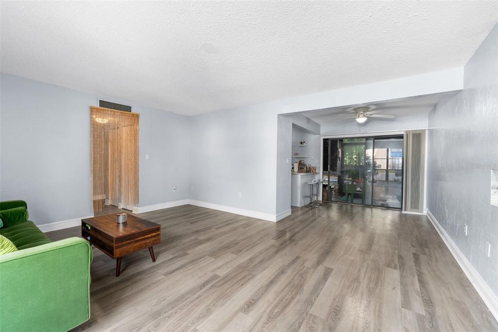 A living room with light gray walls, wood-look flooring, a green sofa, and a sliding door — 2811 SW ARCHER ROAD UNIT P131, GAINESVILLE, FL