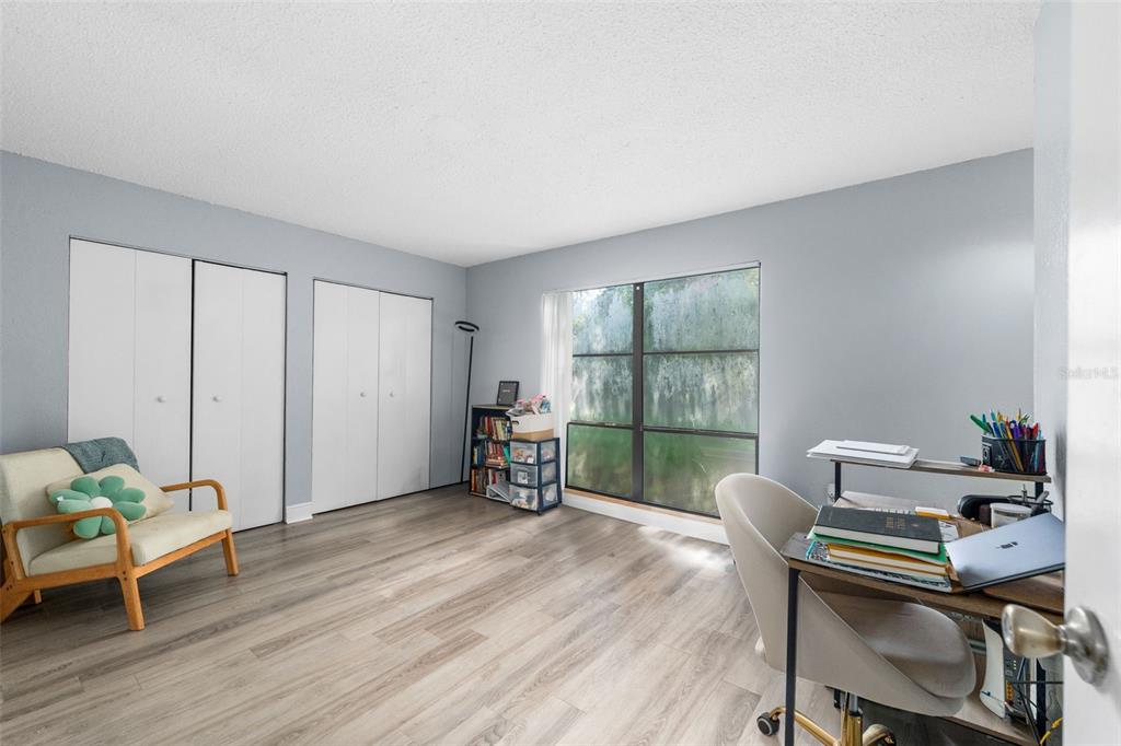 A bedroom with light gray walls, wood-look flooring, two white closets, and a desk area — 2811 SW ARCHER ROAD UNIT P131, GAINESVILLE, FL