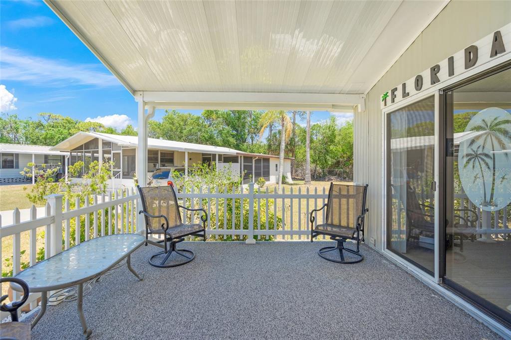 A covered patio with a white fence, two chairs, a table, and a sliding glass door — 925 IGLESIA DRIVE, NORTH PORT, FL