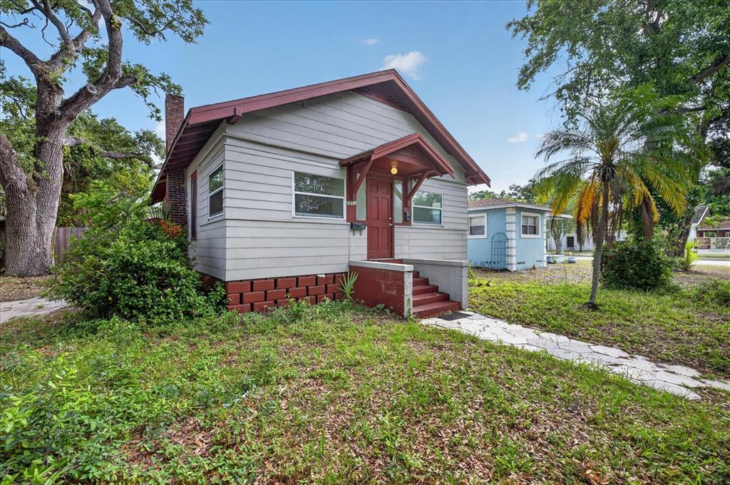 A small, light-gray house with a red door and a brick foundation sits on grass — 2211 22ND AVENUE S, ST PETERSBURG, FL