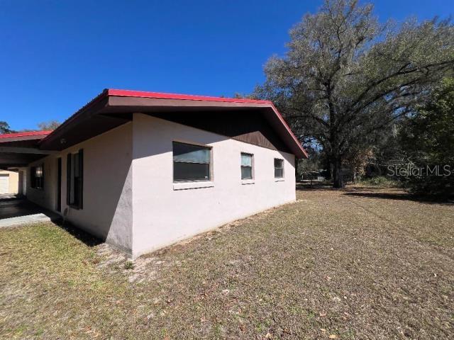 The exterior of a single-story house features a red roof, stucco walls, and a carport — 5875 NE 167TH AVENUE, SILVER SPRINGS, FL