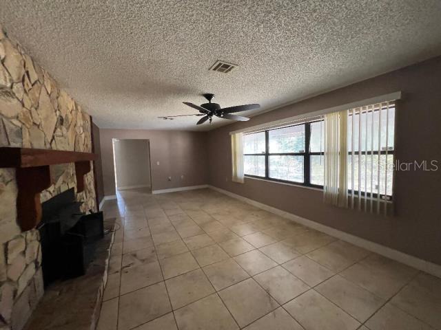 A living room features a stone fireplace, tile flooring, a ceiling fan, and large windows — 5875 NE 167TH AVENUE, SILVER SPRINGS, FL