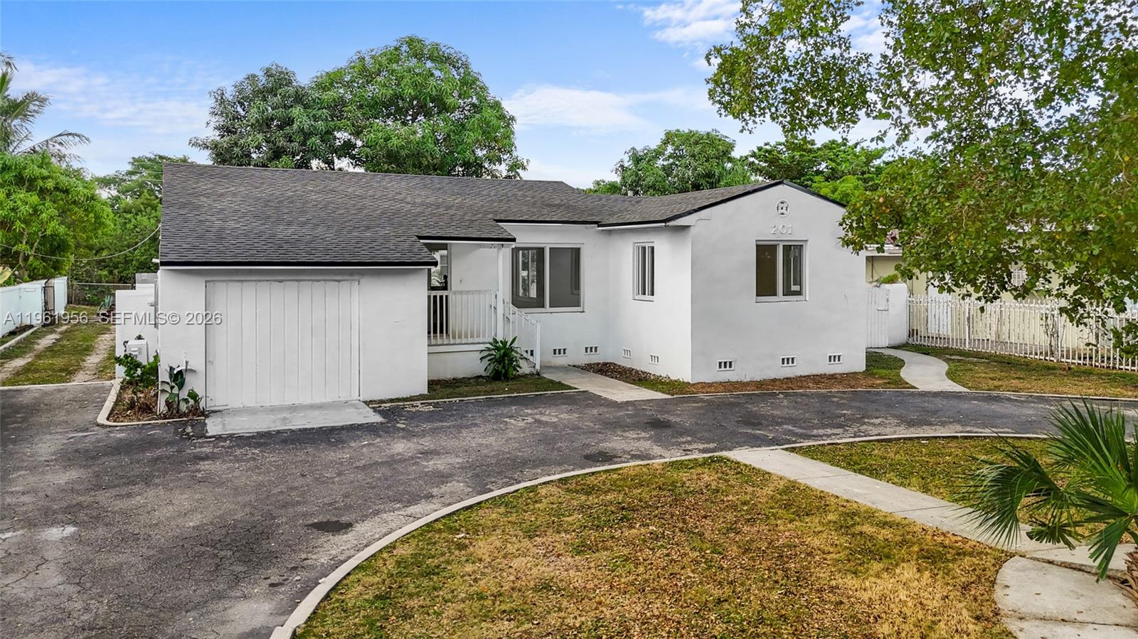 A white single-story house features a dark shingled roof, a garage, and a curved driveway — 201 S Biscayne River Dr, Miami FL 33169, MIAMI, FL