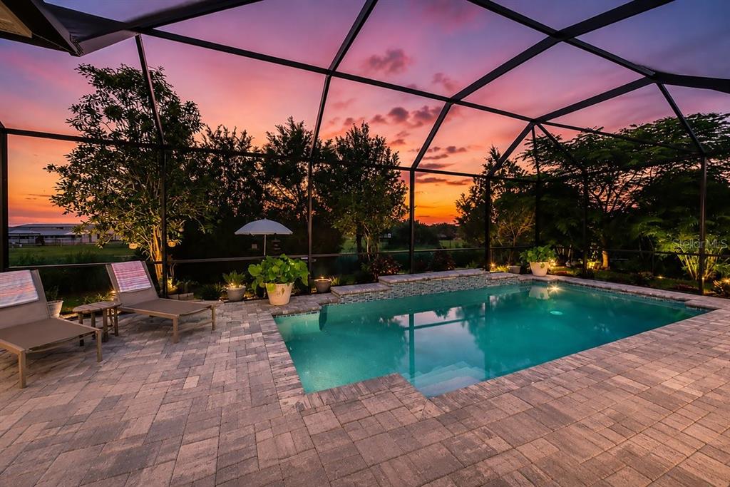 A screened-in patio features a rectangular swimming pool, lounge chairs, and a sunset view — 4657 ANTRIM DRIVE, SARASOTA, FL