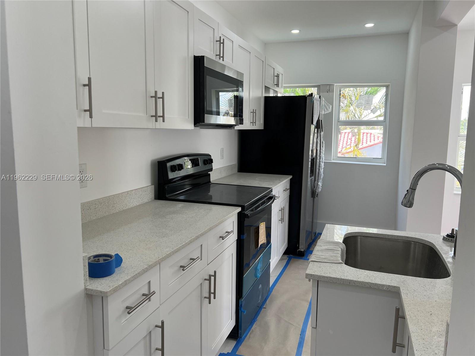 A modern kitchen features white cabinetry, speckled countertops, stainless steel appliances, and a sink — 1015 S 17th Ave # 9, Hollywood FL 33020, HOLLYWOOD, FL
