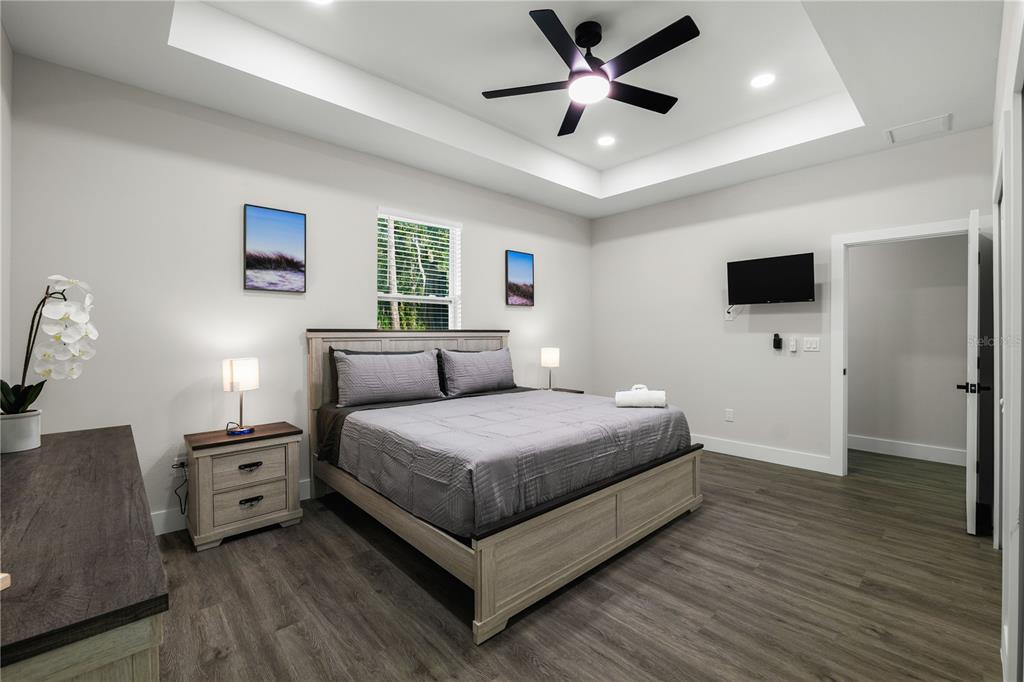 A bedroom features a tray ceiling, a ceiling fan, a bed, and wood-look flooring — 174-176 S LEMON AVENUE, BROOKSVILLE, FL