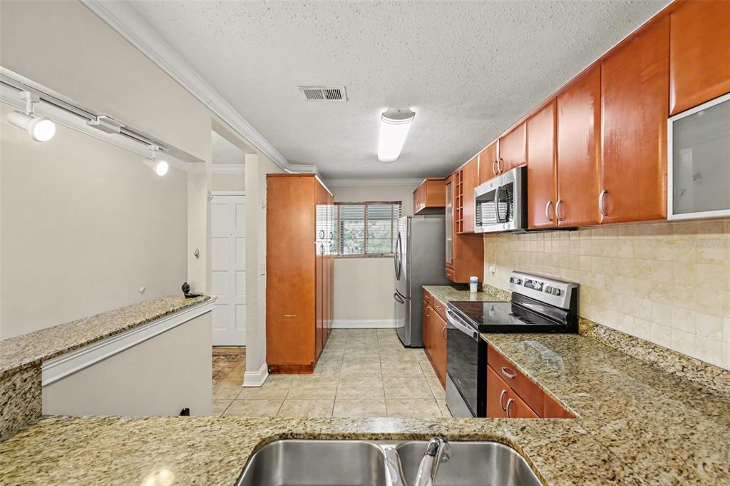 A kitchen features wood cabinets, granite countertops, stainless steel appliances, and tile flooring — 6334 NEWTOWN CIRCLE UNIT 34B3, TAMPA, FL
